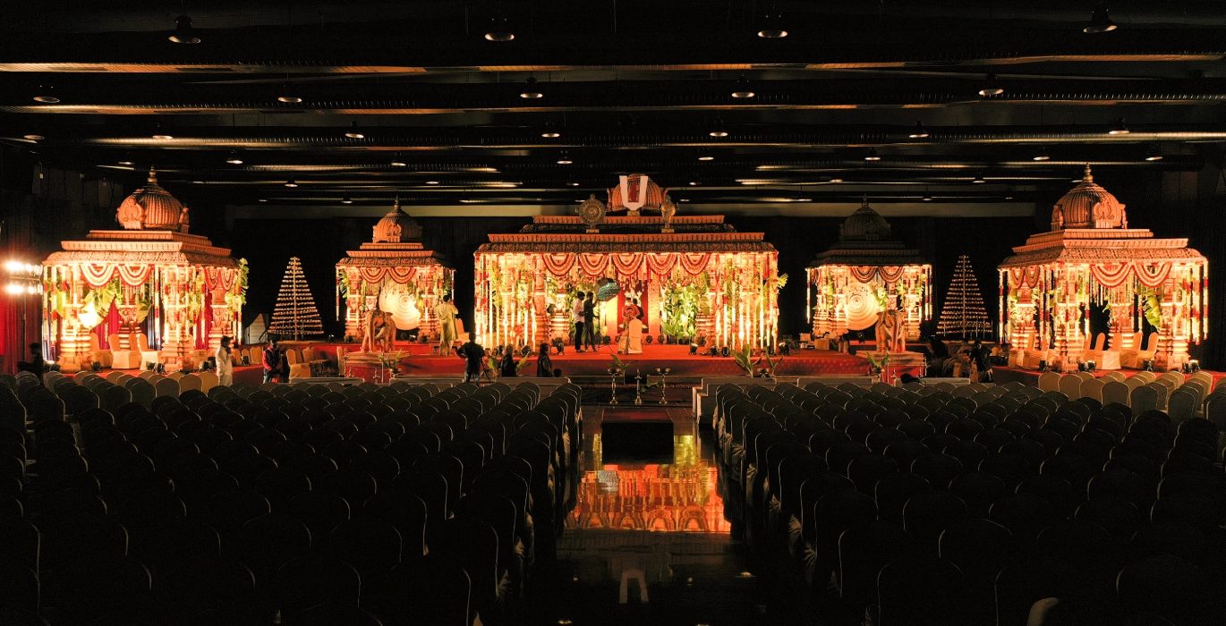 Emerald hall at night with a gold temple-style mandapam lit on the stage and guests seated in front of it